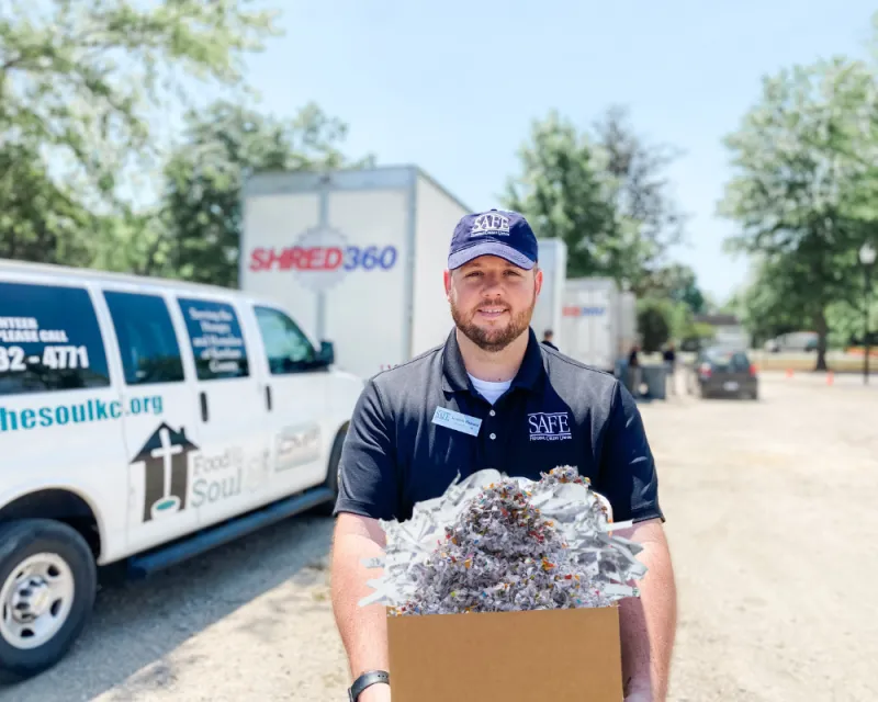 SAFE employee standing in front of shred trucks holding a box of shredded documents.