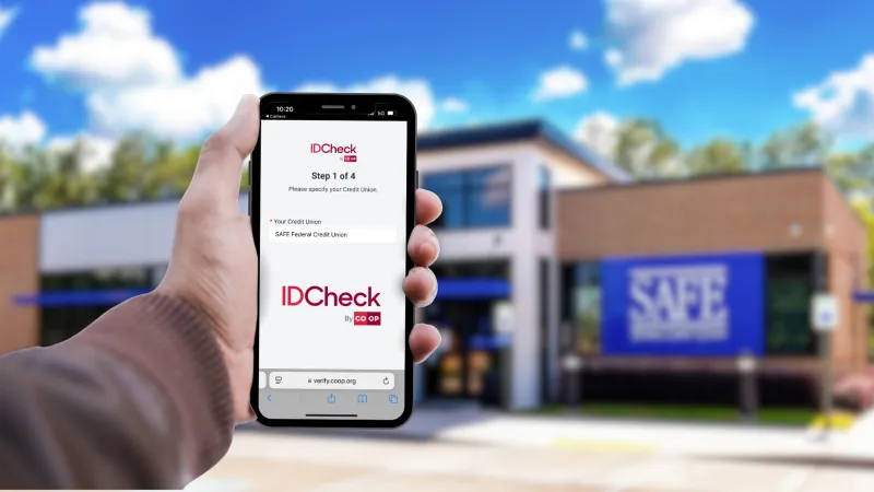 hand holding phone with IDCheck on the screen in front of a SAFE branch.