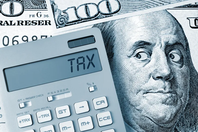 George Benjamin on $100 bill looking at a calculator that says "tax"