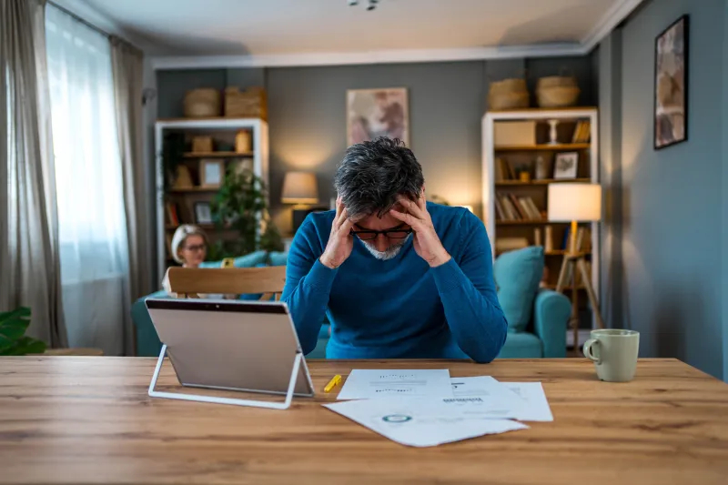 Man looking at bills with his head in his hands.