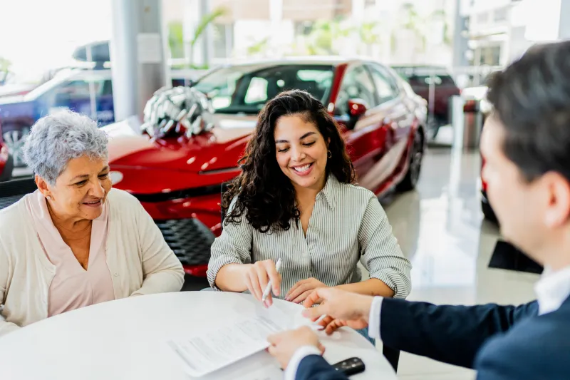 A senior woman signing car paperwork with a younger woman