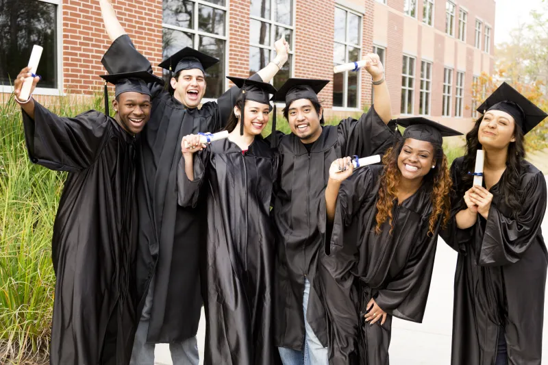 Graduates smiling and holding up diplomas