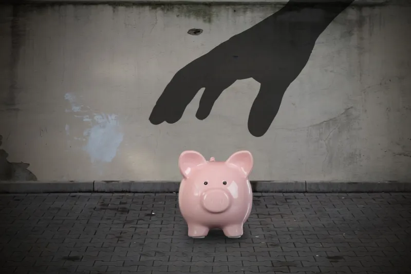 pink piggy bank with a shadow hand over it