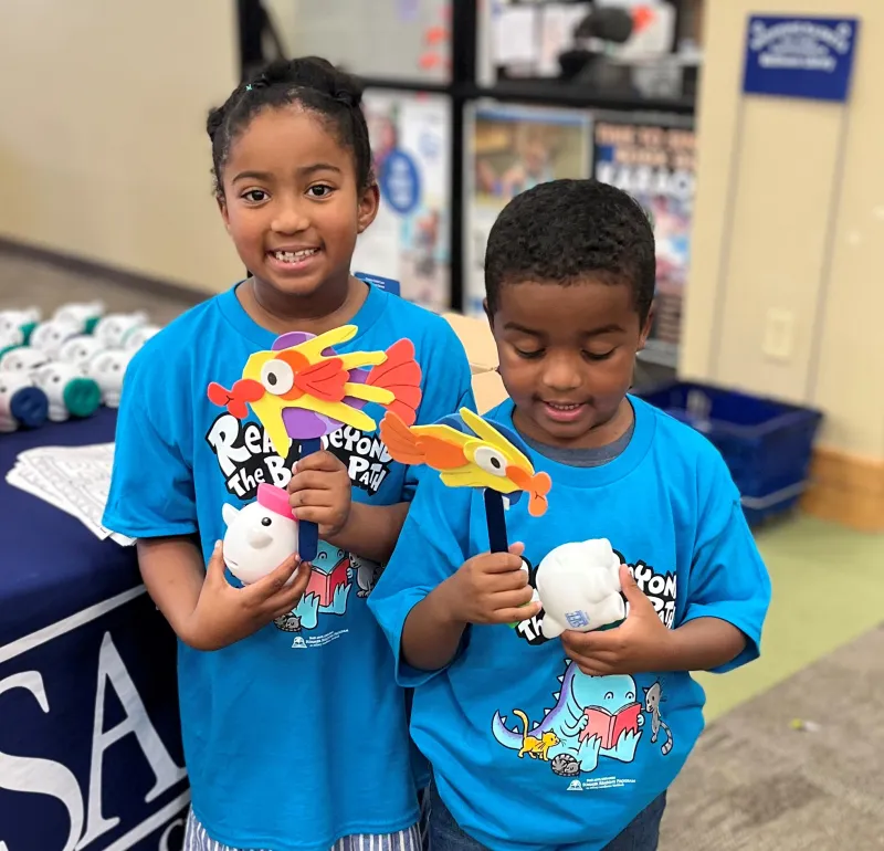 Two children wearing blue shirts holding up their artwork.