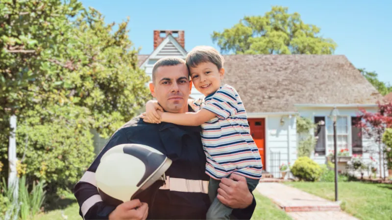 Firefighter holding young son, standing in front of home