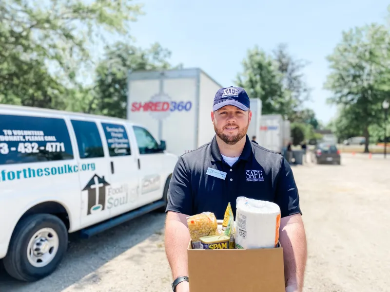 SAFE employee standing in front of shred trucks holding a box of donations