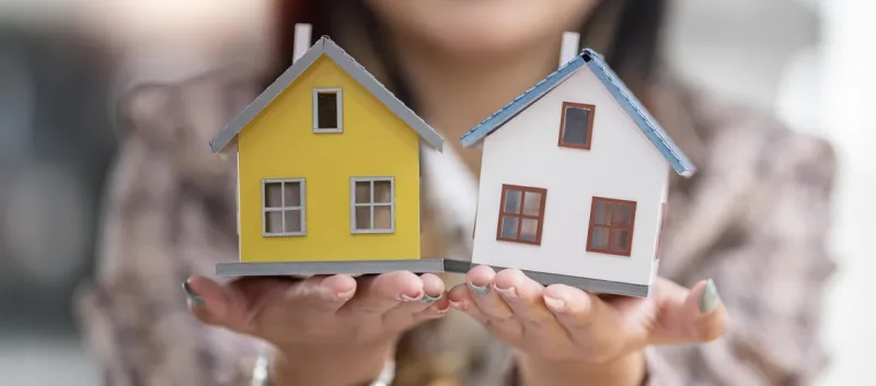 woman holding two small houses. One is yellow and the other is white.