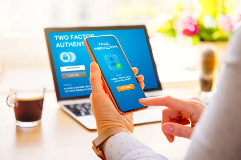 hand holding smart phone with laptop in the background