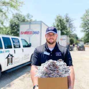 SAFE employee standing in front of shred trucks holding a box of shredded documents.