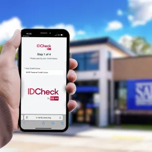 hand holding phone with IDCheck on the screen in front of a SAFE branch.