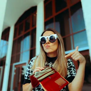 girl wearing glasses pointing at her wallet with money in it.