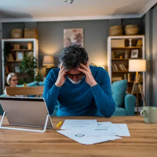 Man looking at bills with his head in his hands.