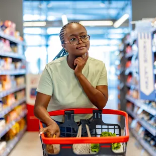 woman walking a grocery store aisle with a thoughtful look on her face.