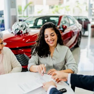 A senior woman signing car paperwork with a younger woman