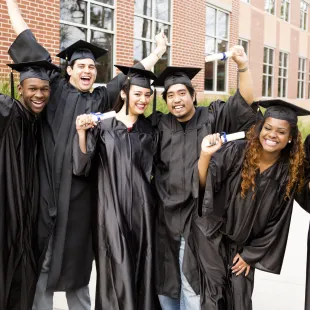 Graduates smiling and holding up diplomas