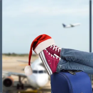 photo of shoes and a santa hat propped op on a suitcase at the airport.