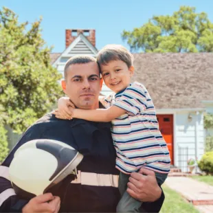 Firefighter holding young son, standing in front of home