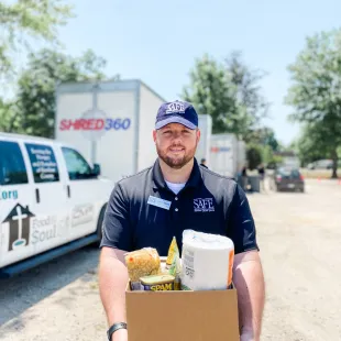 SAFE employee standing in front of shred trucks holding a box of donations