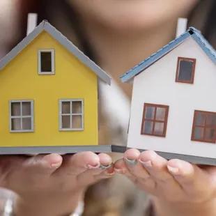 woman holding two small houses. One is yellow and the other is white.