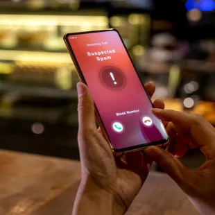 A person holding a phone that says "Suspected Spam."