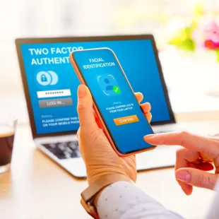 hand holding smart phone with laptop in the background